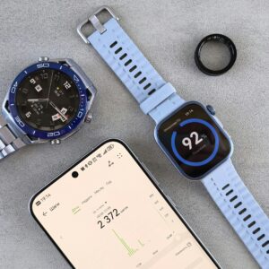 Home Smartwatch, ring tracker, and smartphone displaying fitness data on a gray surface.